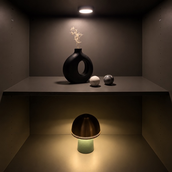 A black vase and ornaments on a display shelf, with a table lamp below